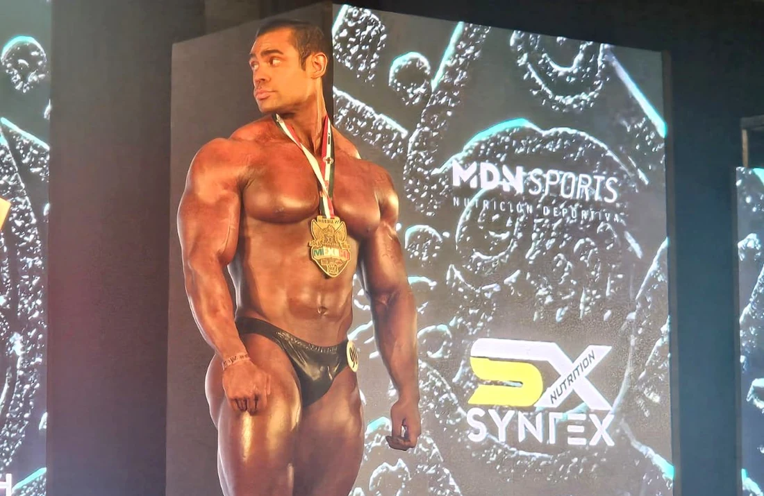 Athlete with a Mr. México medal on stage beside the Syntex Nutrition logo